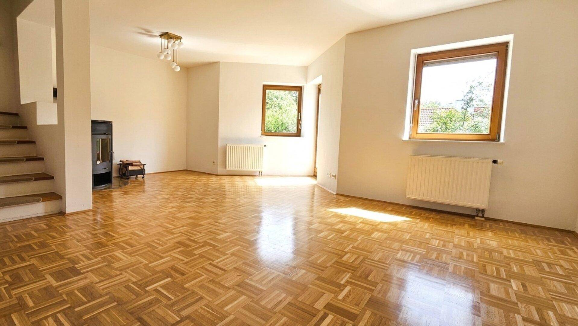 Helles Wohnzimmer mit Parkettboden, Kaminofen und Zugang zu einer Treppe.