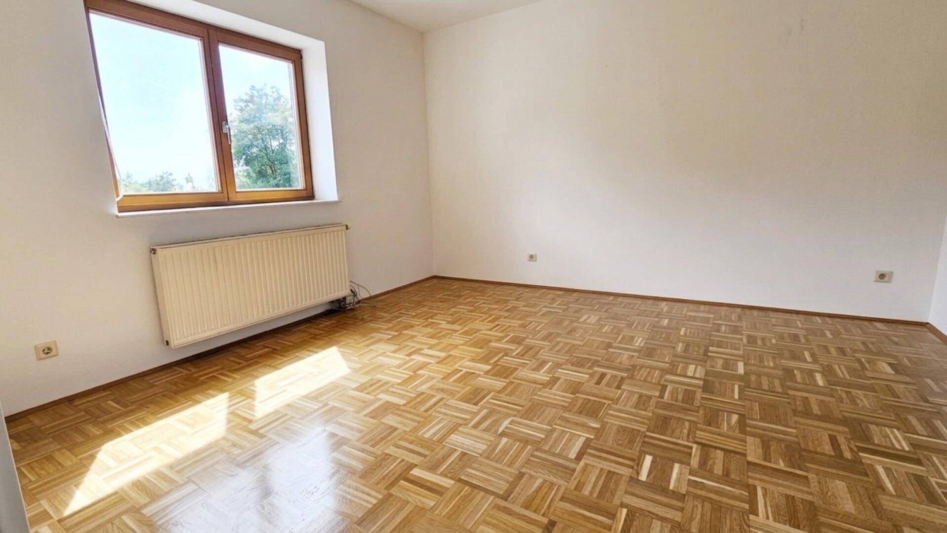 Helles Schlafzimmer mit Parkettboden und einem Fenster, das viel Tageslicht hereinlässt.