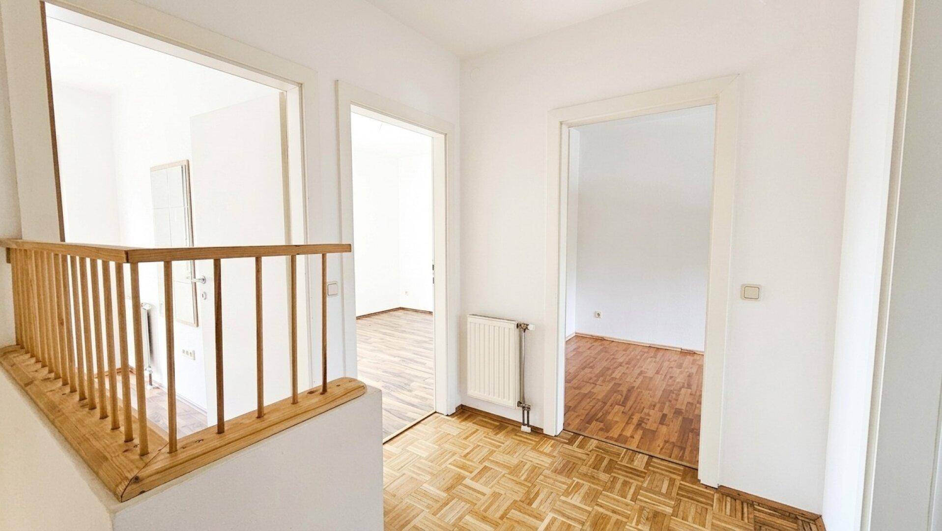 Heller Flur im Obergeschoss mit Parkettboden und Holzgeländer, verbindet mehrere Räume.