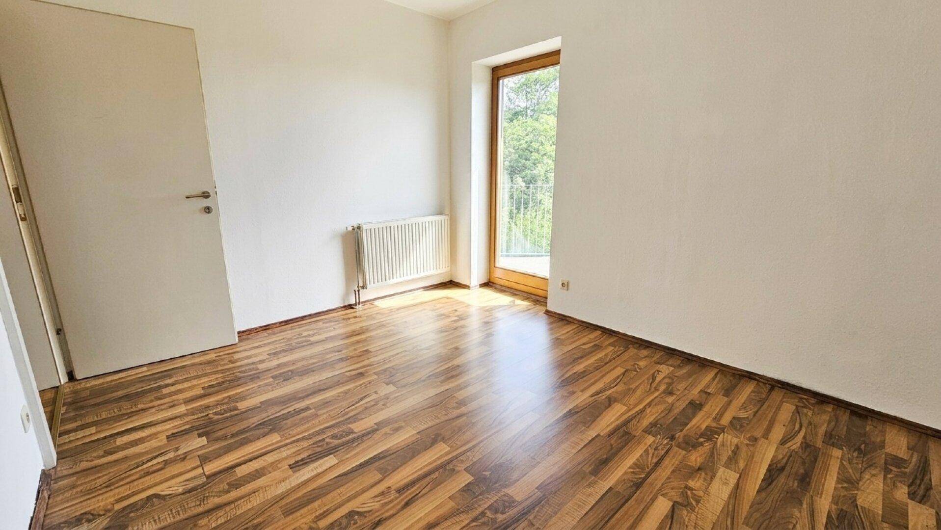 Helles Zimmer mit Laminatboden und Zugang zu einem französischen Balkon.