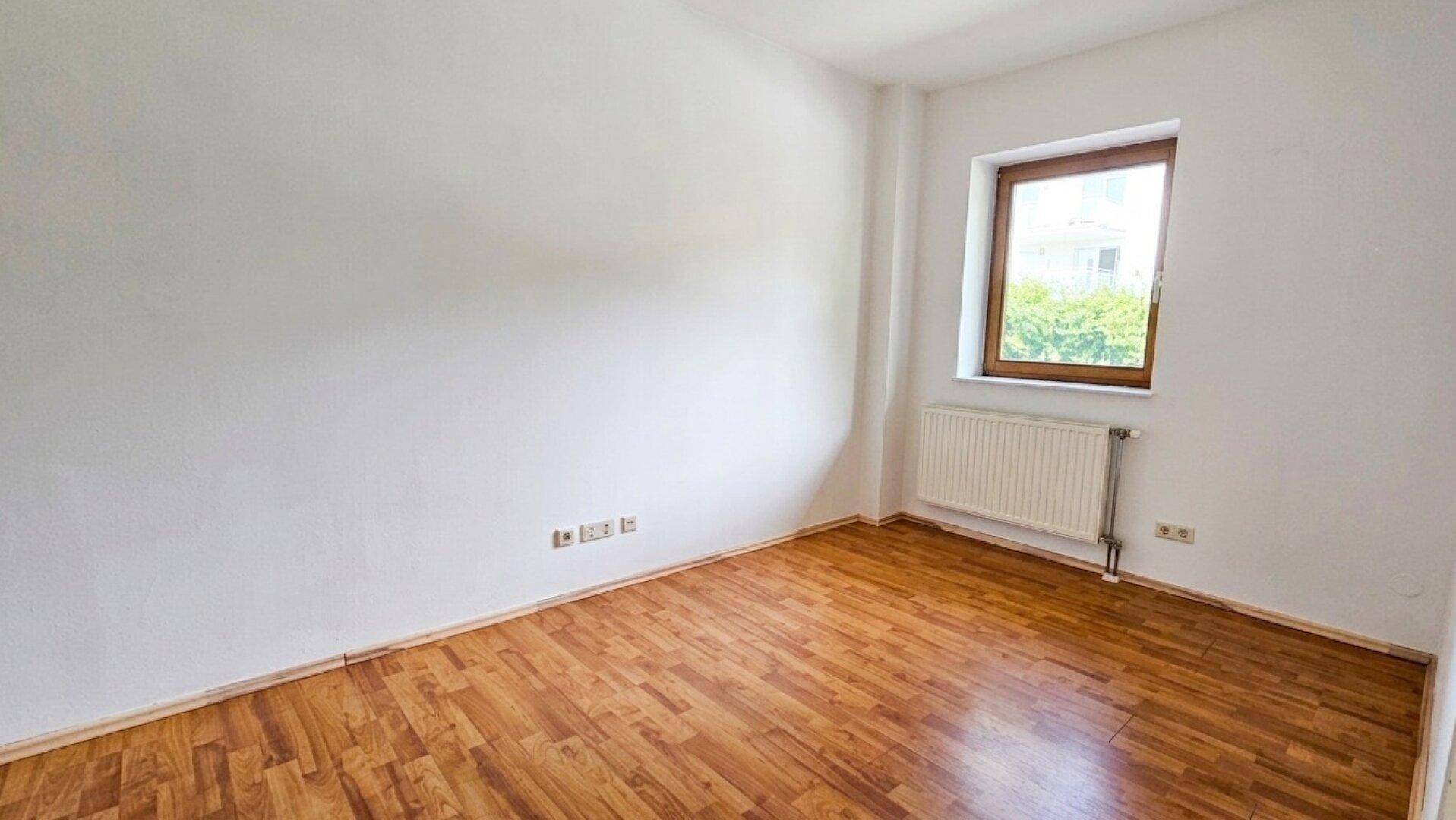 Schlafzimmer mit Laminatboden und einem Fenster, das für ausreichend Helligkeit sorgt.