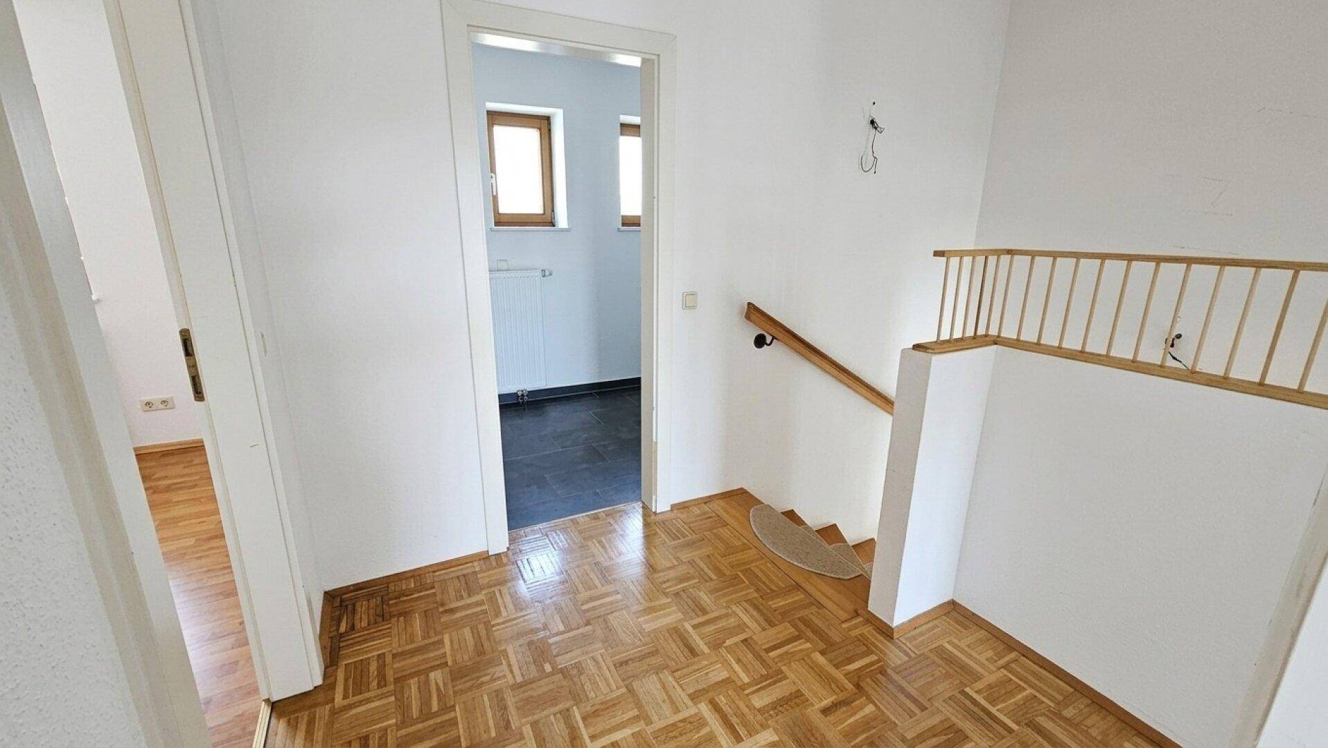 Flur im Obergeschoss mit Parkettboden und Treppenaufgang, führt zu weiteren Zimmern.