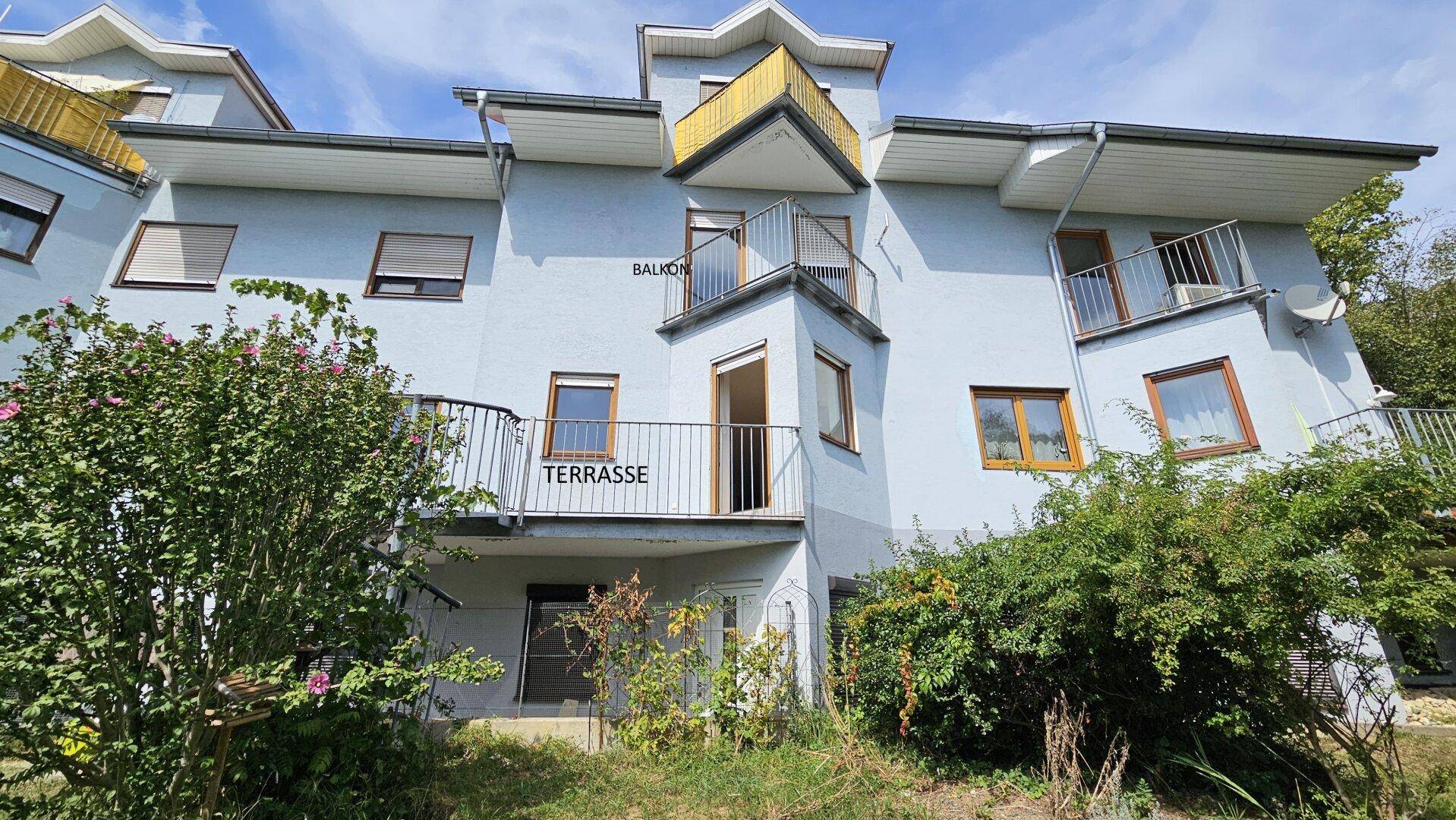 Fassade eines hellblauen Gebäudes mit mehreren Balkonen und einer Terrasse.