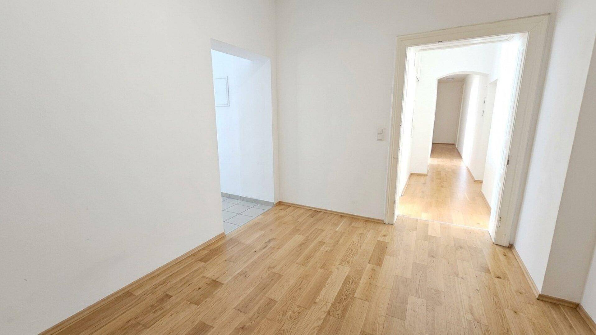Heller Flur mit Holzboden und weißen Wänden, der zu weiteren Räumen führt.