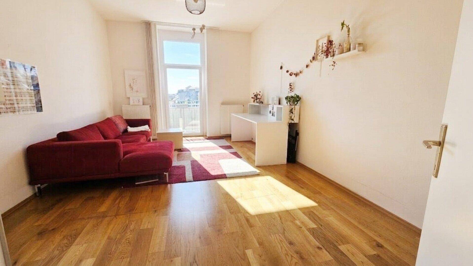 Helles Wohnzimmer mit rotem Sofa, Holzboden und großem Fenster, das viel Tageslicht hereinlässt.