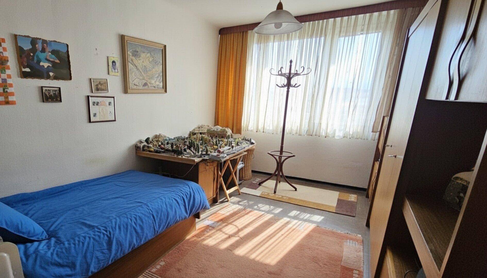 Helles Kinder- oder Gästezimmer mit Einzelbett, Schreibtisch und großem Fenster.