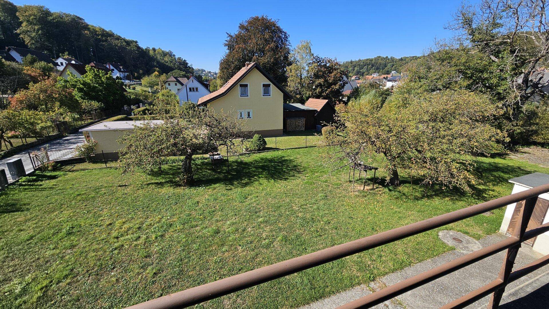 Weitläufiger Blick vom Balkon über den großen Garten mit Obstbäumen und die umliegende Landschaft.