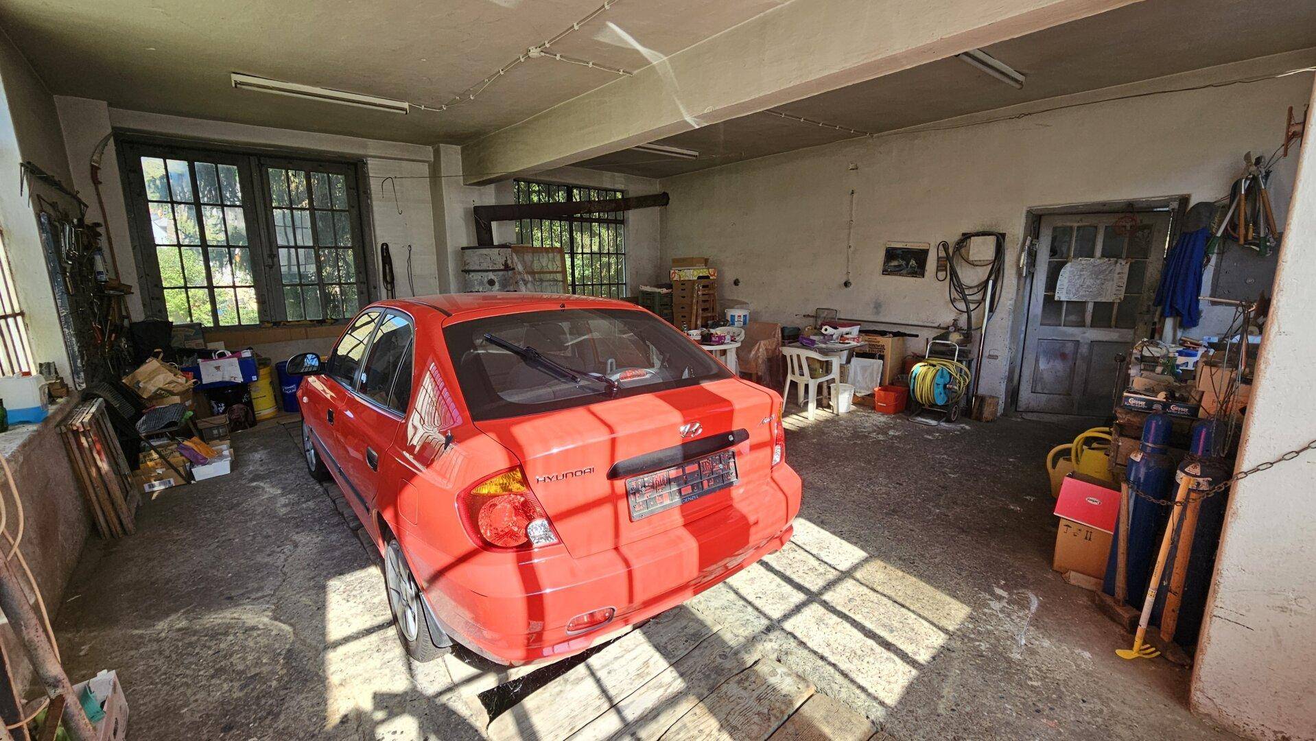 Große Garage mit Betonboden, viel Stauraum und einem geparkten roten Auto.