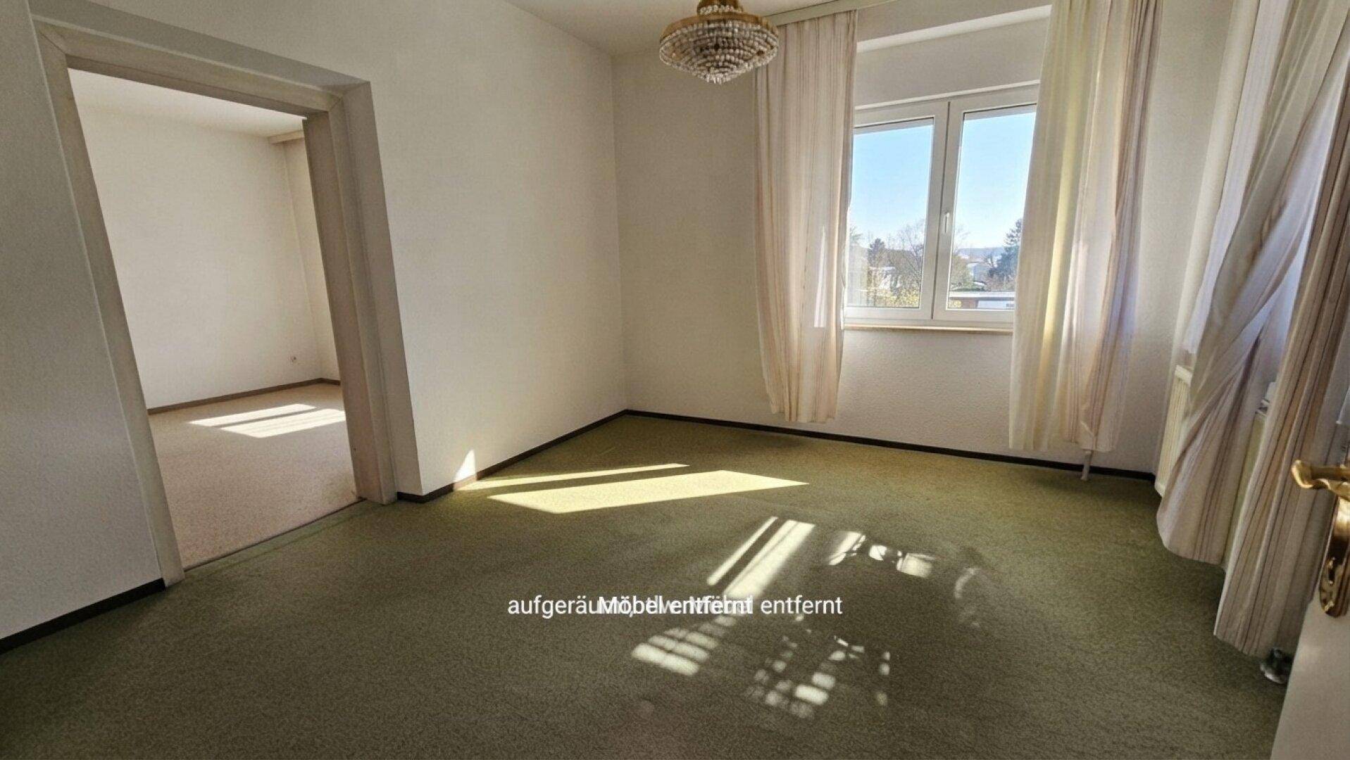 Helles Wohnzimmer mit grünem Teppichboden, großen Fenstern und Blick ins Grüne.