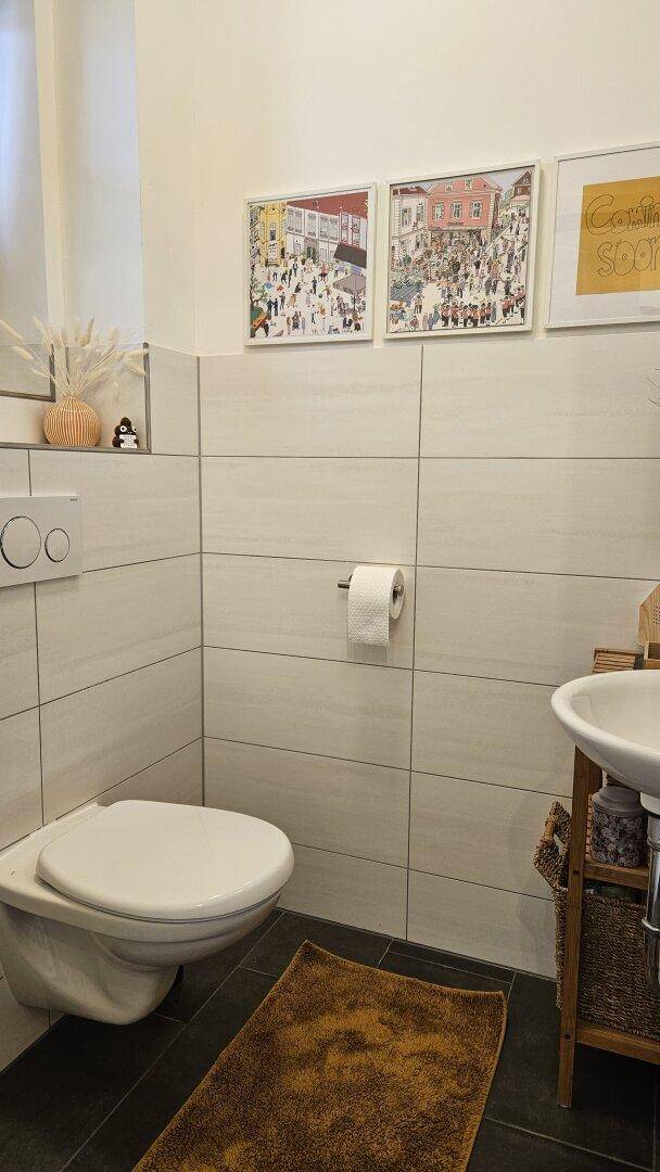 Gäste-WC mit Wand-WC, Waschbecken und modernen Fliesen an den Wänden.