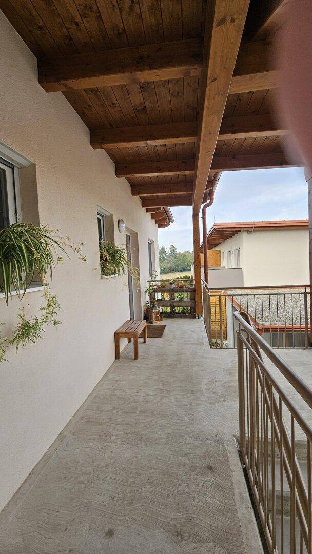 Überdachter Balkon mit Holzbalken und Geländer, bietet einen Blick ins Grüne.