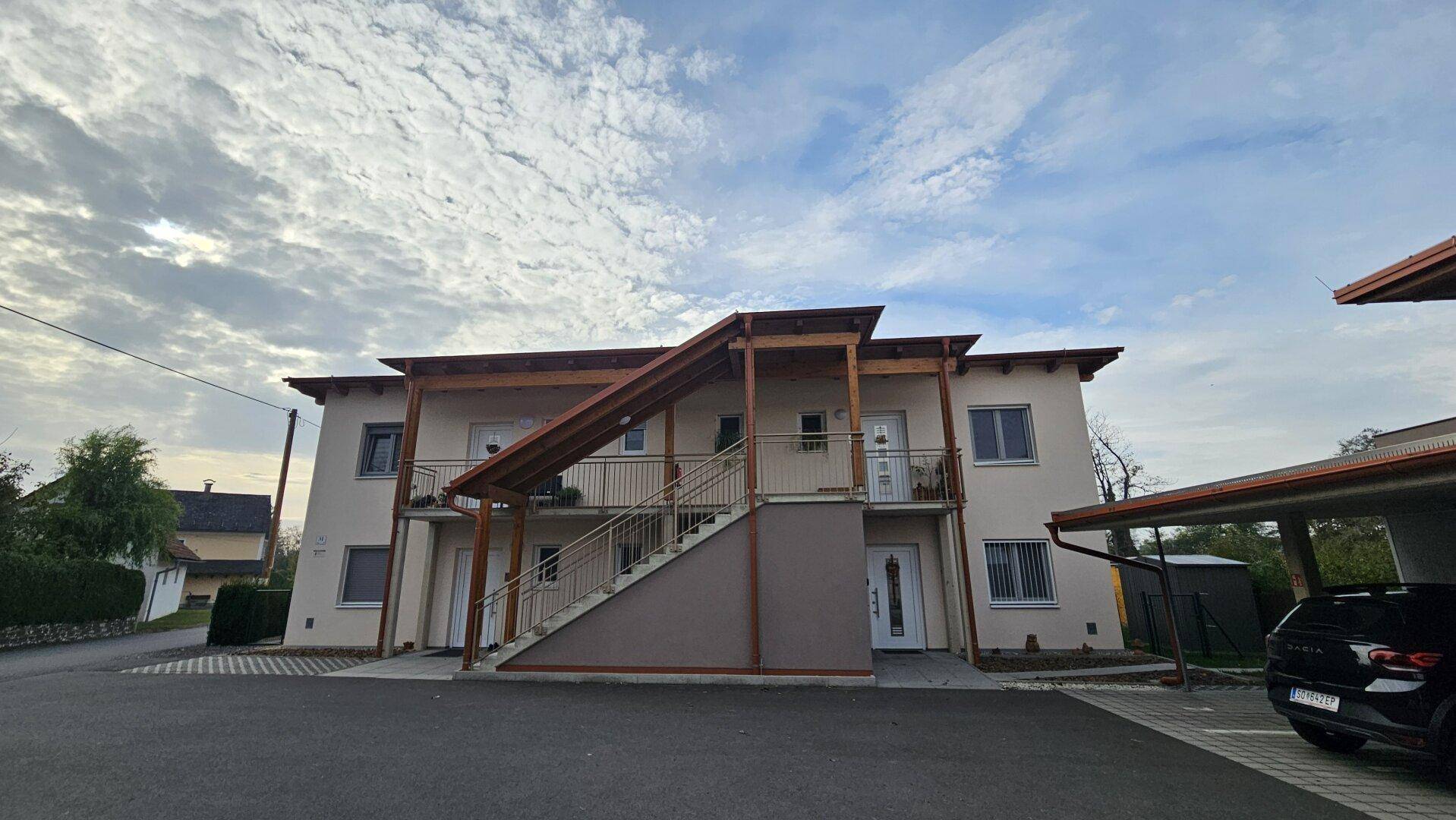 Modernes Mehrfamilienhaus mit Holzdetails, Außentreppe und Carport-Parkplätzen.