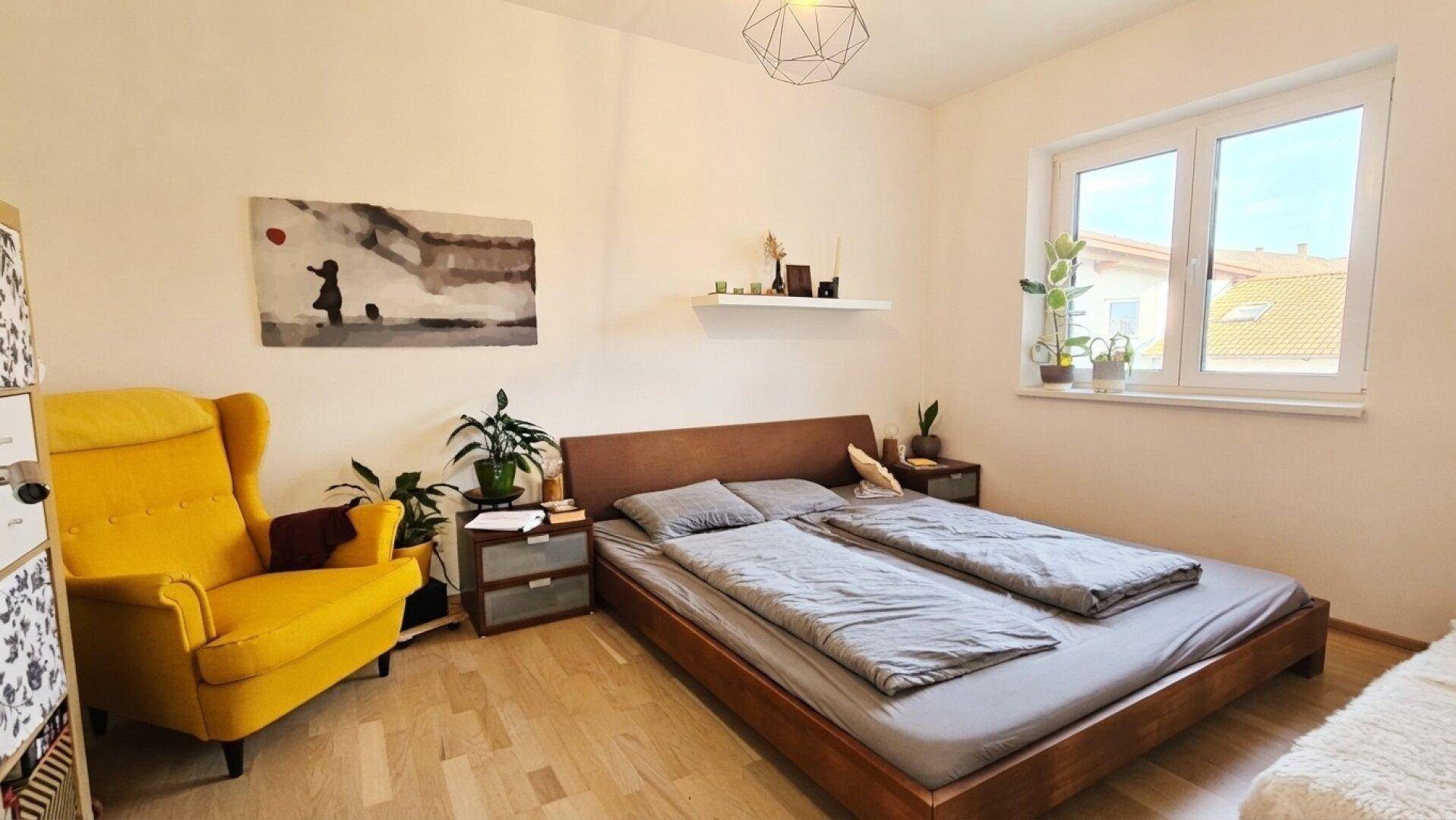 Gemütliches Schlafzimmer mit Holzbett, Parkettboden und großem Fenster für viel Licht.