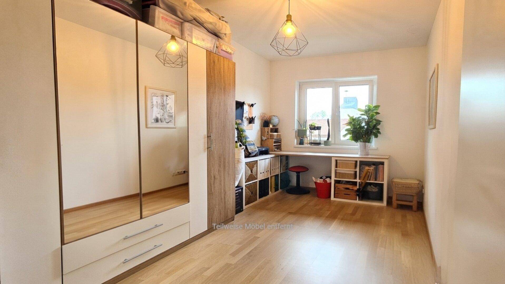 Helles Arbeitszimmer mit großem Schreibtisch, Spiegelschrank und Parkettboden.