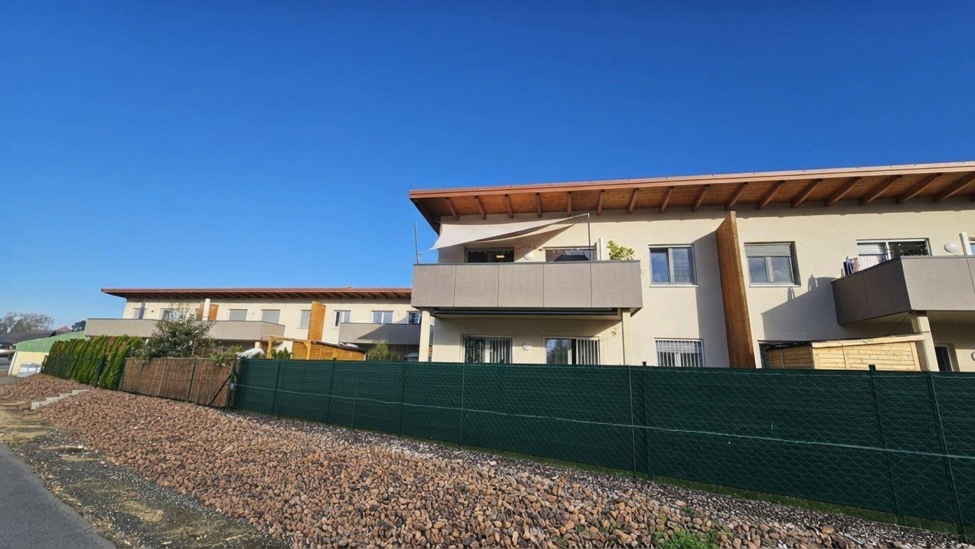 Moderne Wohngebäude mit Balkonen und grüner Umzäunung in ländlicher Umgebung.