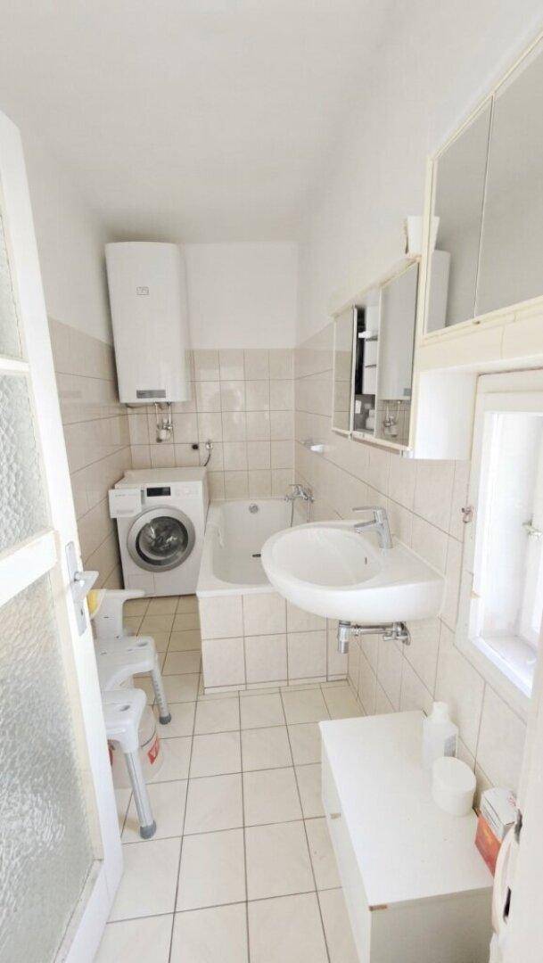 Gefliestes Badezimmer mit Badewanne, Waschbecken, Waschmaschine und Fenster.