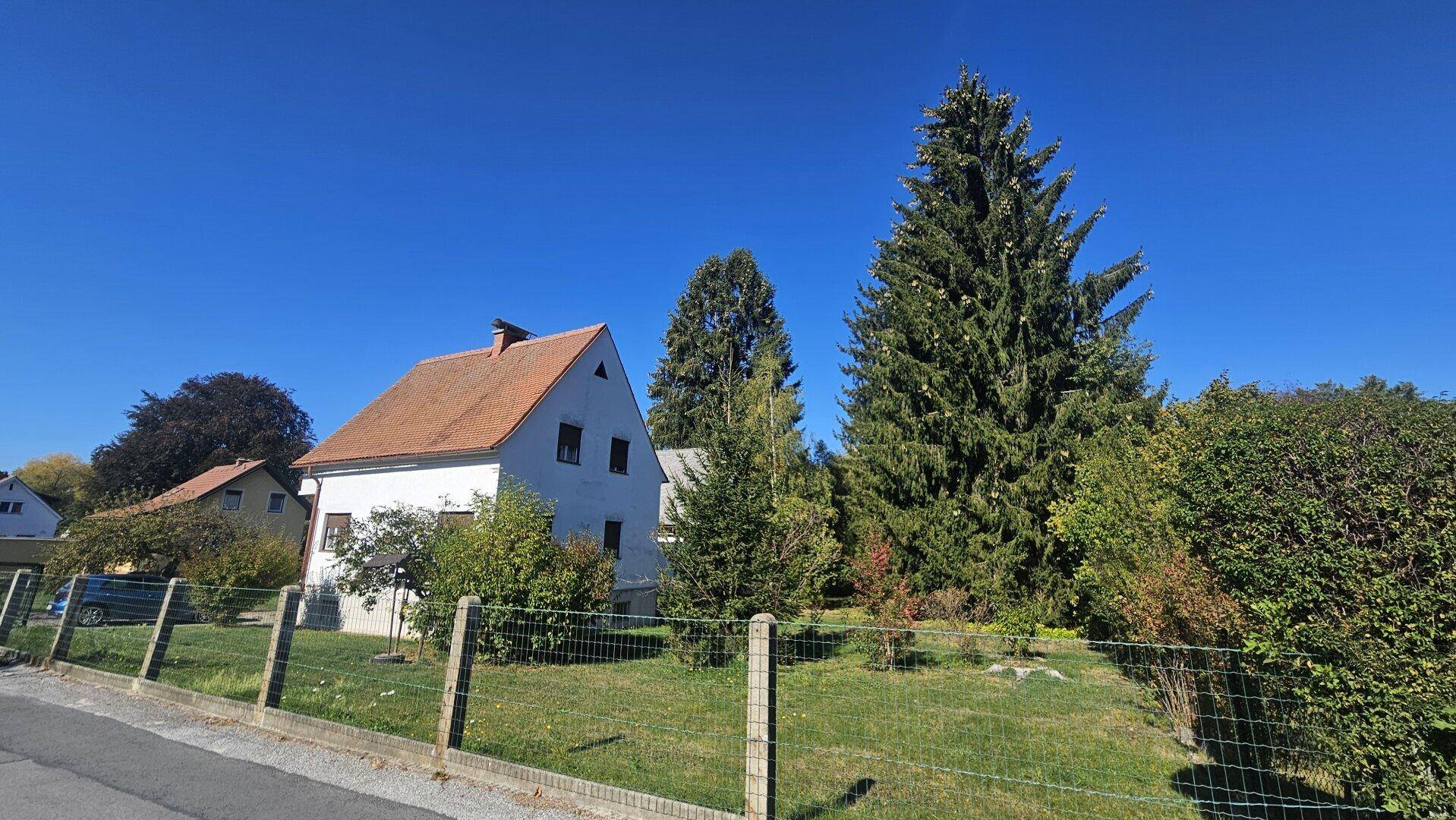 Weißes Haus mit orangefarbenem Dach, umgeben von Bäumen und einem grünen Garten.