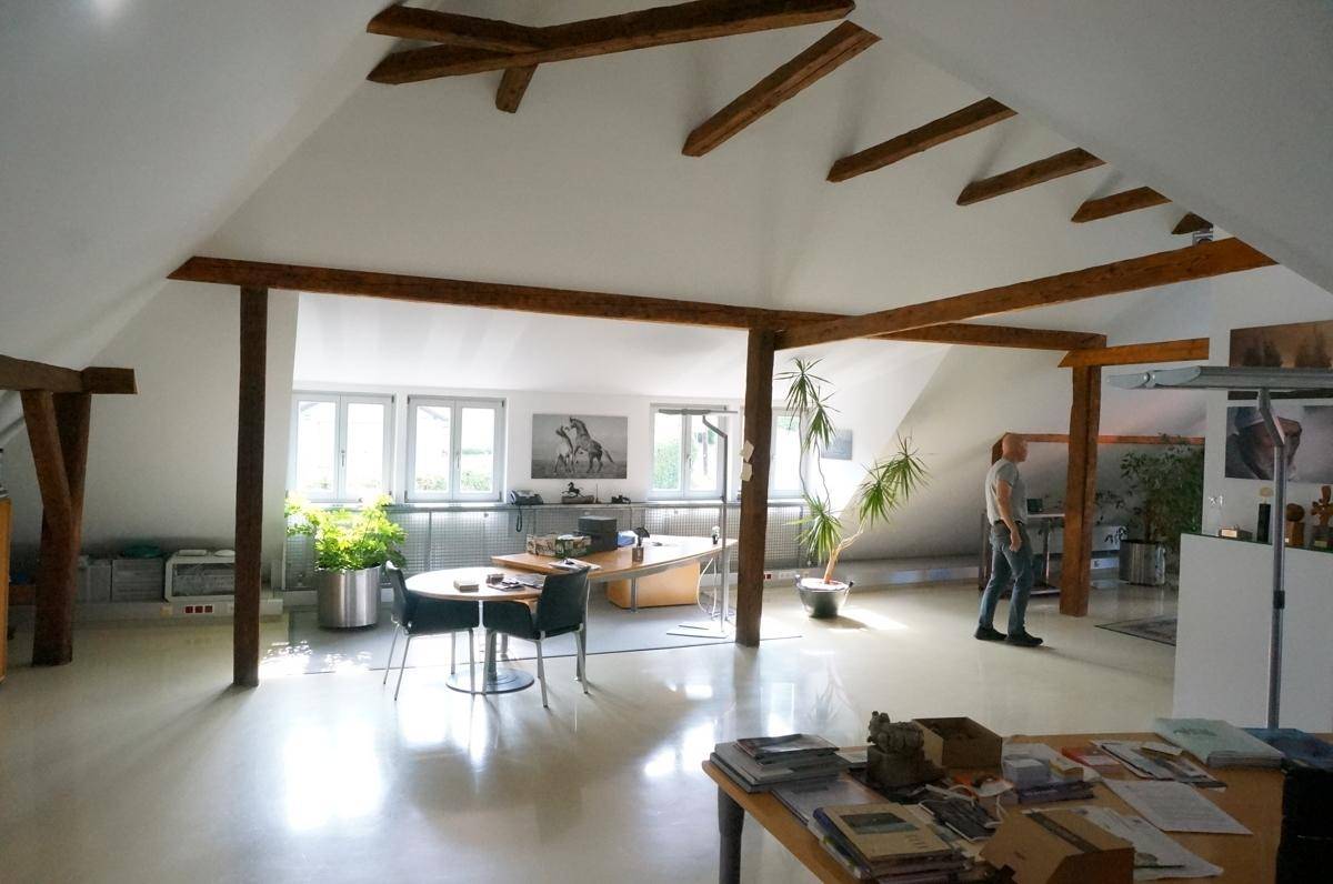 Helles Dachgeschossbüro mit schrägen Wänden, Holzbalken und funktionalen Arbeitsbereichen.