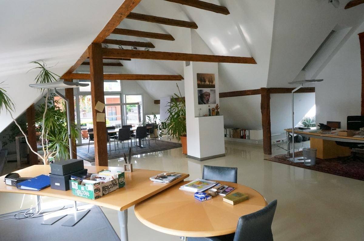 Offener Bürobereich im Dachgeschoss mit verschiedenen Arbeitsplätzen und Holzbalken.