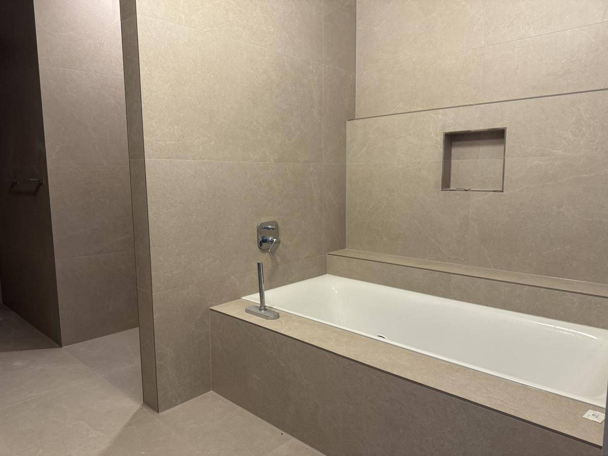 Modernes Badezimmer mit einer eleganten, eingebauten Badewanne und hochwertigen grauen Fliesen.