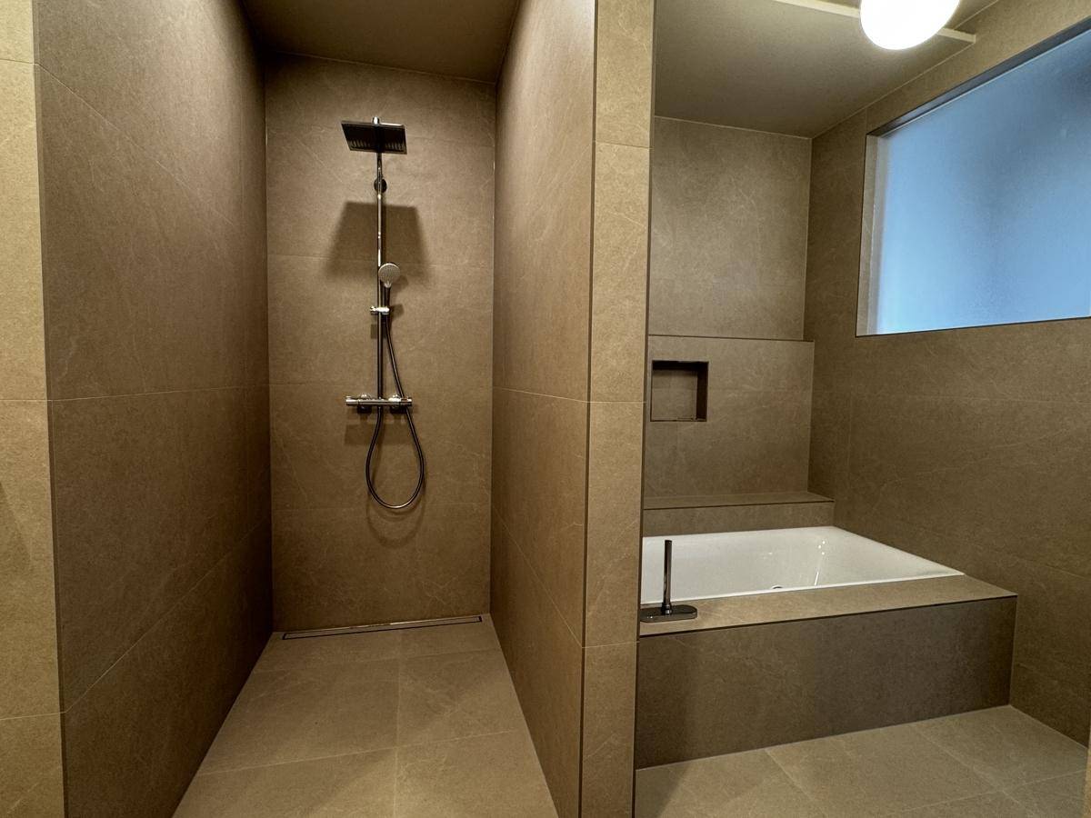 Elegantes Badezimmer mit begehbarer Dusche und integrierter Badewanne, komplett gefliest in Grau.