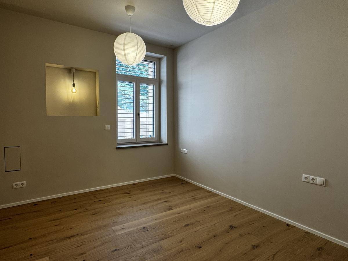 Helles Zimmer mit Holzboden, großem Fenster und modernen Deckenleuchten.