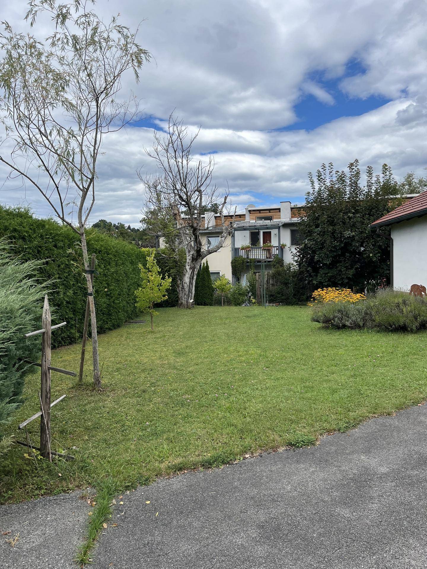 Weitläufiger Garten mit Rasenfläche und Blick auf ein Wohnhaus im Hintergrund unter blauem Himmel.