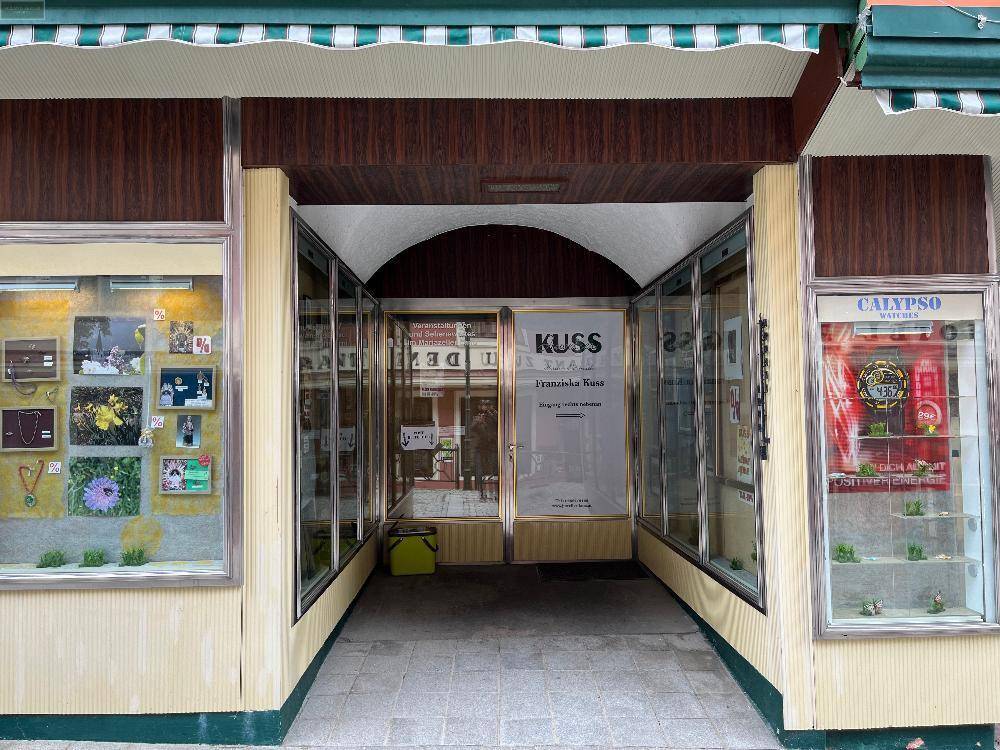 Eingangsbereich eines Geschäfts mit großen Schaufenstern und einem gewölbten Durchgang in der Fassade.