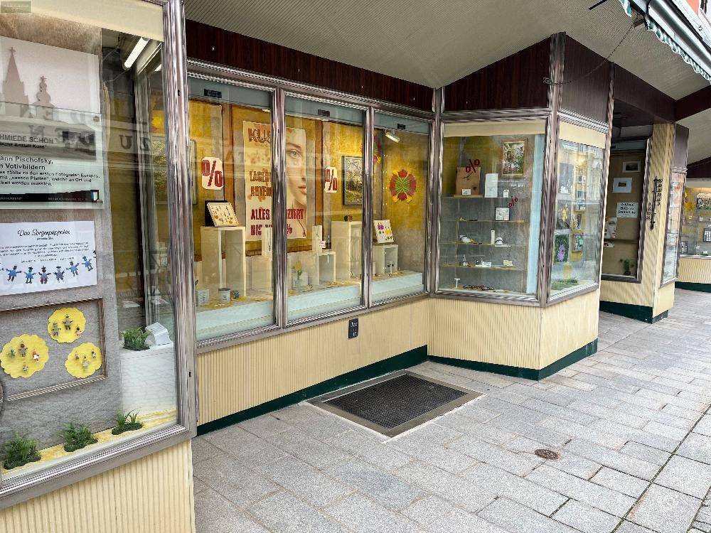 Schaufenster eines Geschäfts mit Auslagen und einem gepflasterten Gehweg davor in der Altstadt.