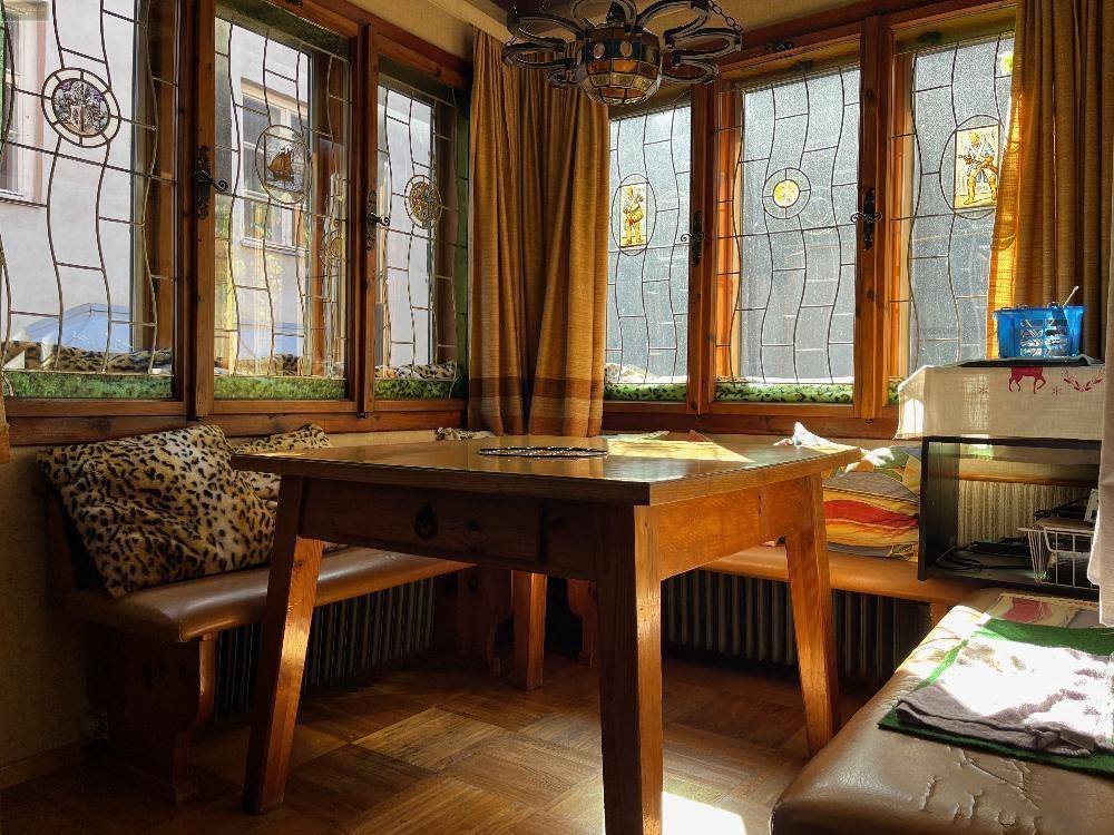 Heller Wintergarten mit Buntglasfenstern, Holztisch und Sitzbank, durchflutet von Sonnenlicht.