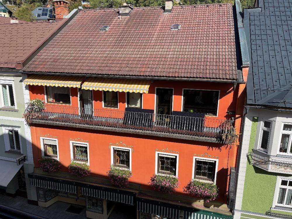 Dachansicht eines orangefarbenen Gebäudes mit Ziegeldach und Balkon in einer städtischen Umgebung.