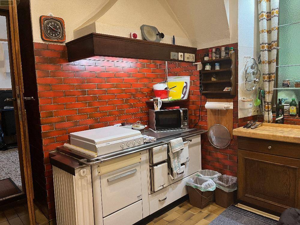 Traditionelle Küche mit Backsteinwand, Holzherd und Regalen für Gewürze, strahlt Gemütlichkeit aus.