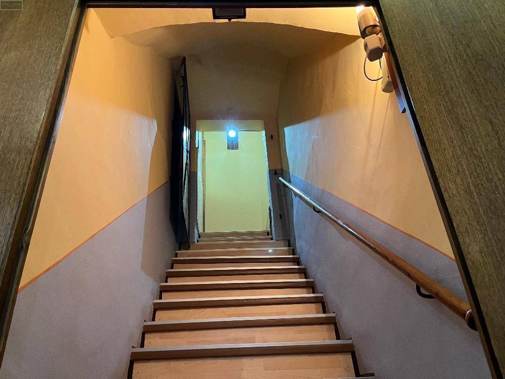 Treppenhaus mit Holzstufen und gelb-grau gestrichenen Wänden, führt in einen oberen Bereich des Hauses.