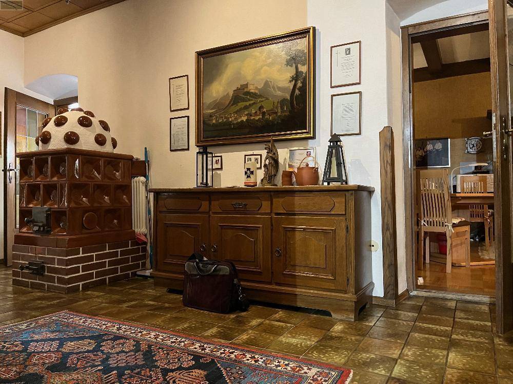 Wohnbereich mit traditionellem Kachelofen, Holzkommode und gemustertem Teppich, schafft eine warme Atmosphäre.