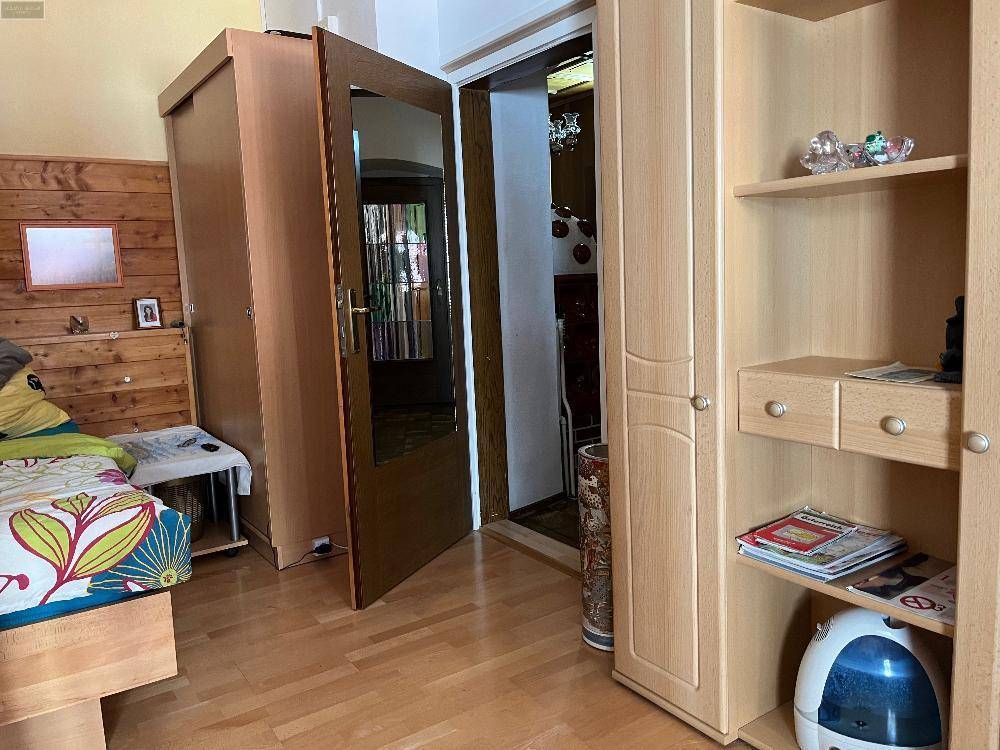 Schlafzimmer mit Holzboden, hellem Kleiderschrank und offener Tür zu einem weiteren Raum.