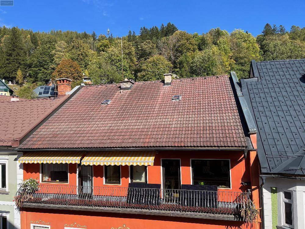 Dachansicht eines orangefarbenen Gebäudes mit Ziegeldach und Balkon, umgeben von grünen Hügeln.