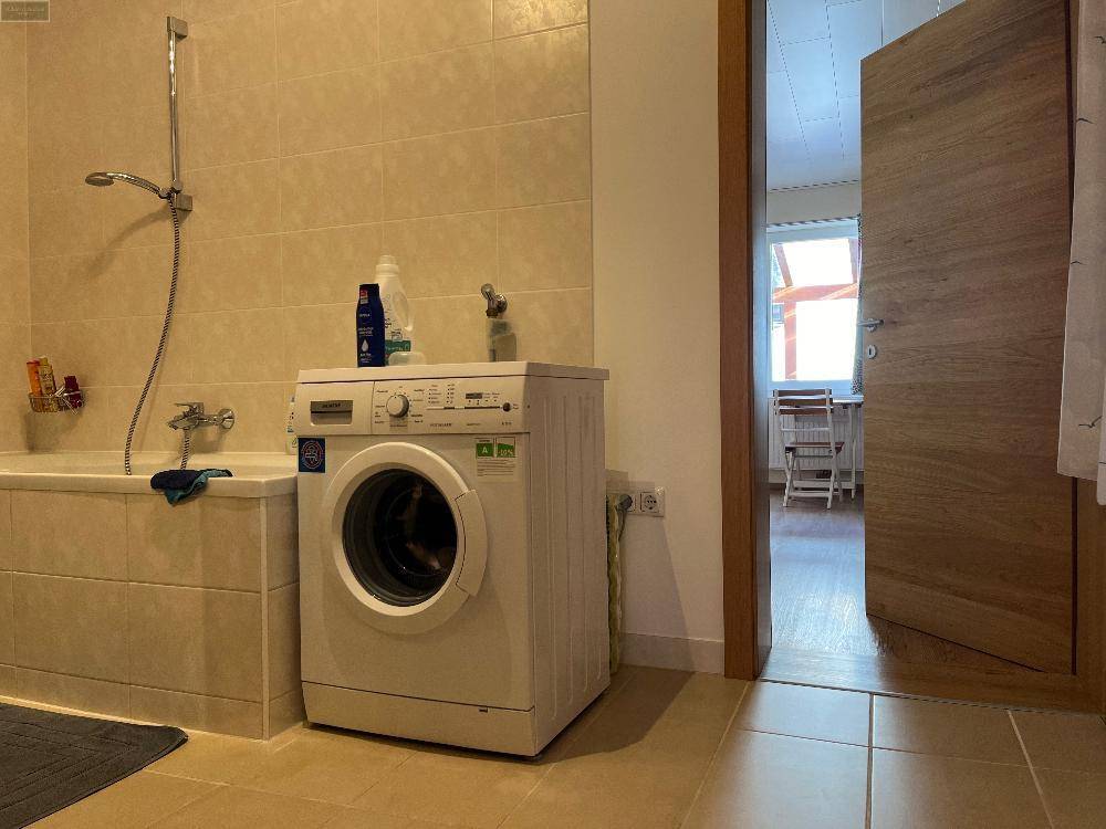 Badezimmer mit beigefarbenen Fliesen, Badewanne und Waschmaschine, praktisch und funktional.