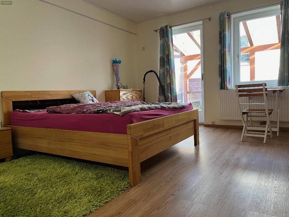 Schlafzimmer mit Holzbett, Holzboden und Zugang zu einem Wintergarten, hell und geräumig.