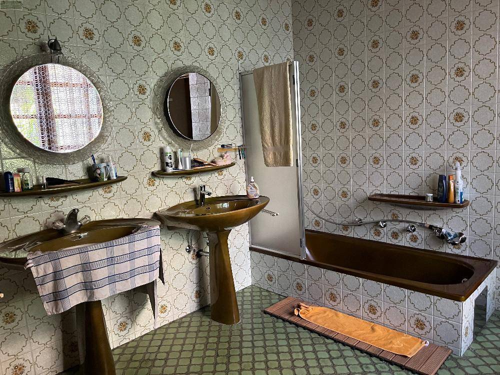 Badezimmer mit gemusterten Fliesen, zwei Waschbecken und einer Badewanne in Braun, im 80er-Jahre-Stil.