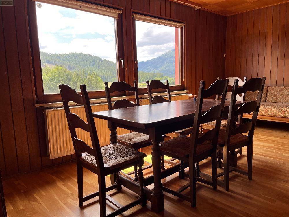 Rustikaler Essbereich mit Holztisch, passenden Stühlen und weitem Blick auf die bewaldeten Berge.