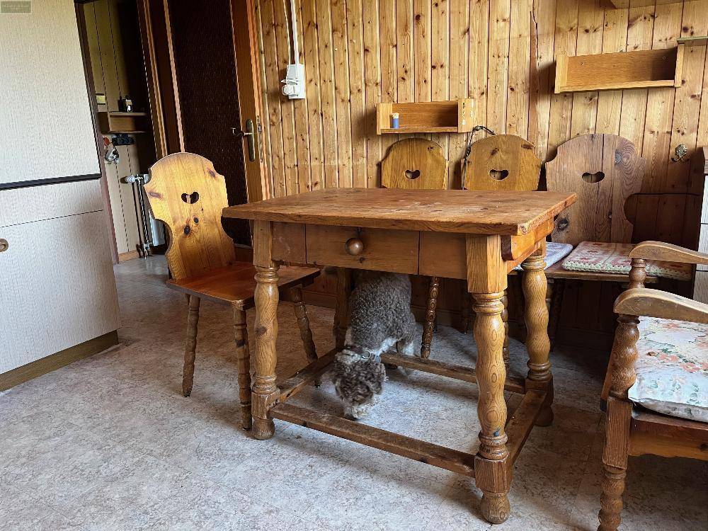 Gemütlicher Essbereich in der Küche mit traditionellen Holzmöbeln und einem Hund unter dem Tisch.