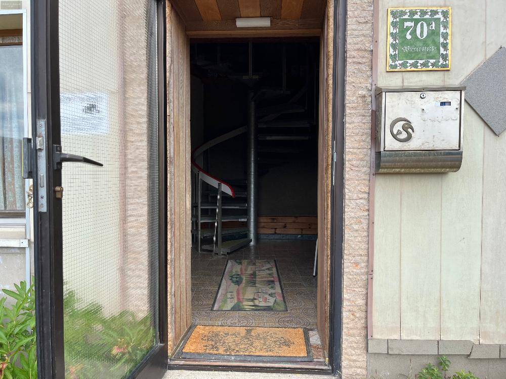 Eingangsbereich mit offener Tür, die den Blick auf eine Wendeltreppe im Inneren freigibt.