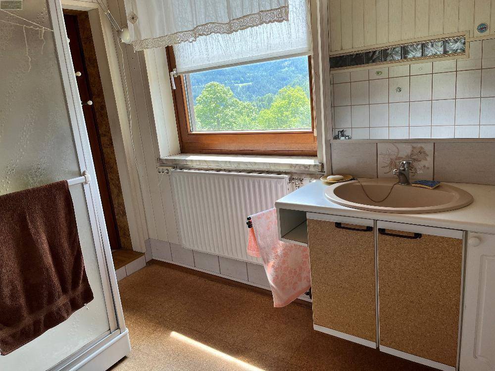 Badezimmer mit Waschbecken, Spiegelschrank und Fenster mit Blick ins Grüne.