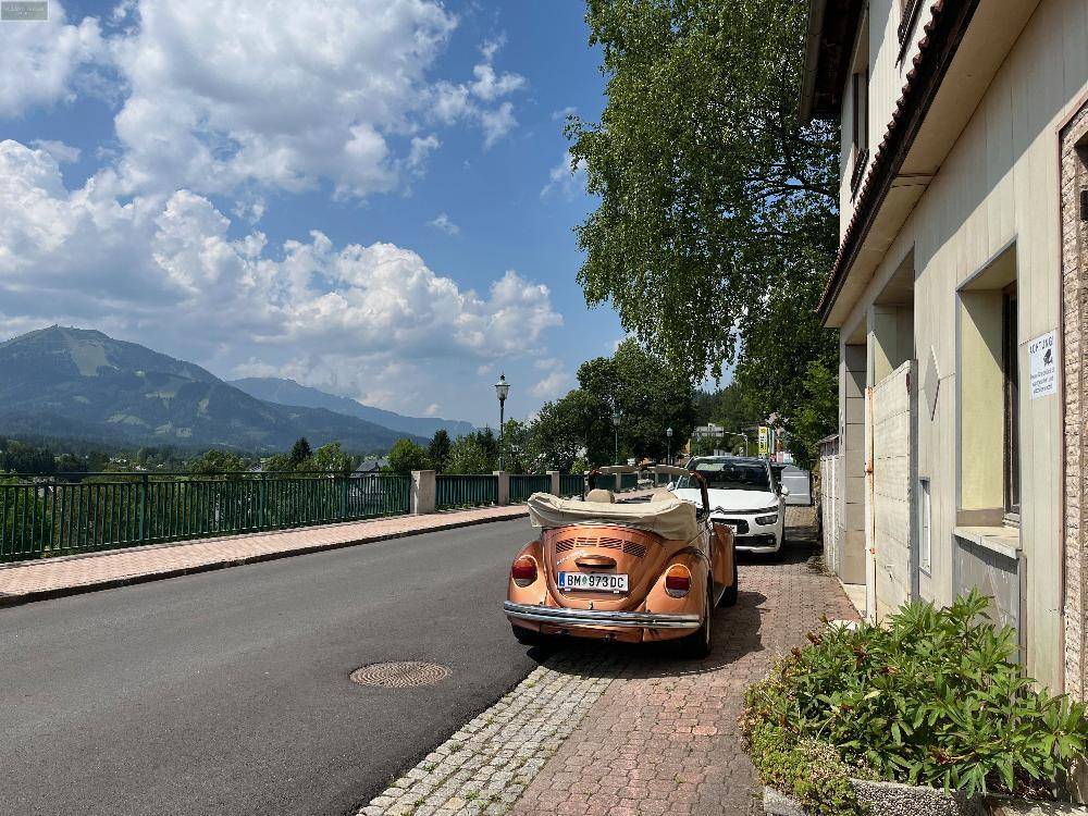 Blick auf die Straße mit einem geparkten Oldtimer und einer malerischen Berglandschaft im Hintergrund.