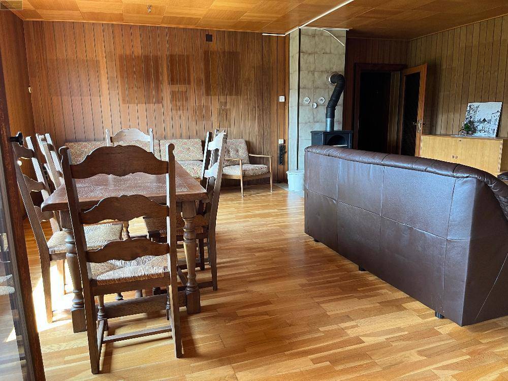 Geräumiger Wohn-Essbereich mit Holzvertäfelung, großem Esstisch, Ledersofa und einem Holzofen.