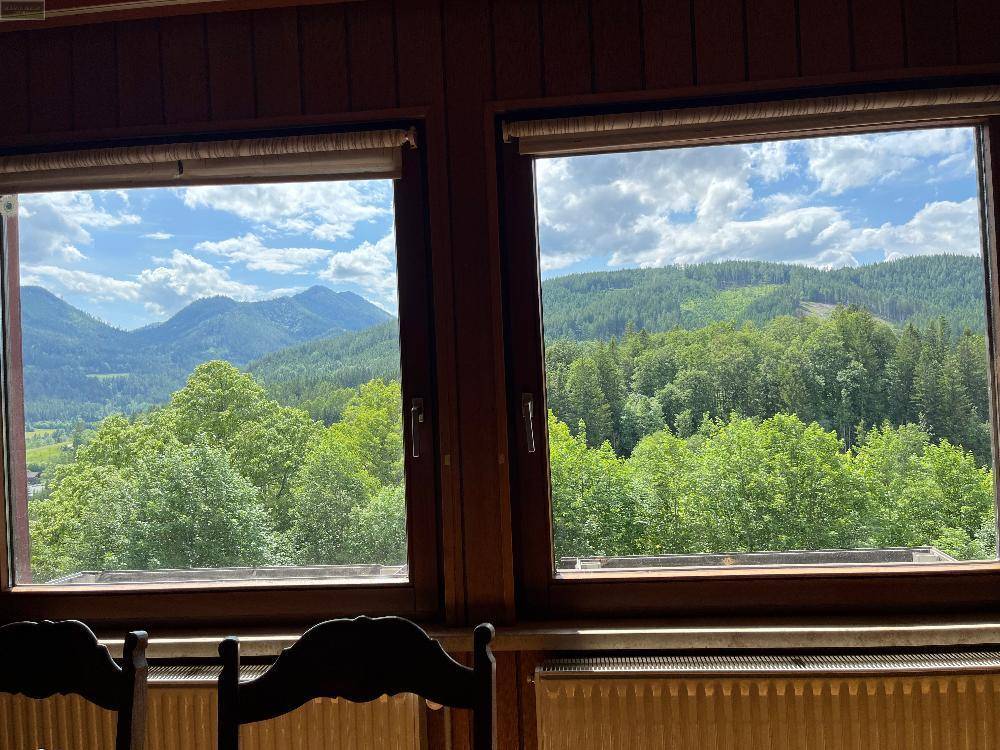 Panoramablick aus zwei Fenstern auf eine weite grüne Landschaft mit Wäldern und Bergen.