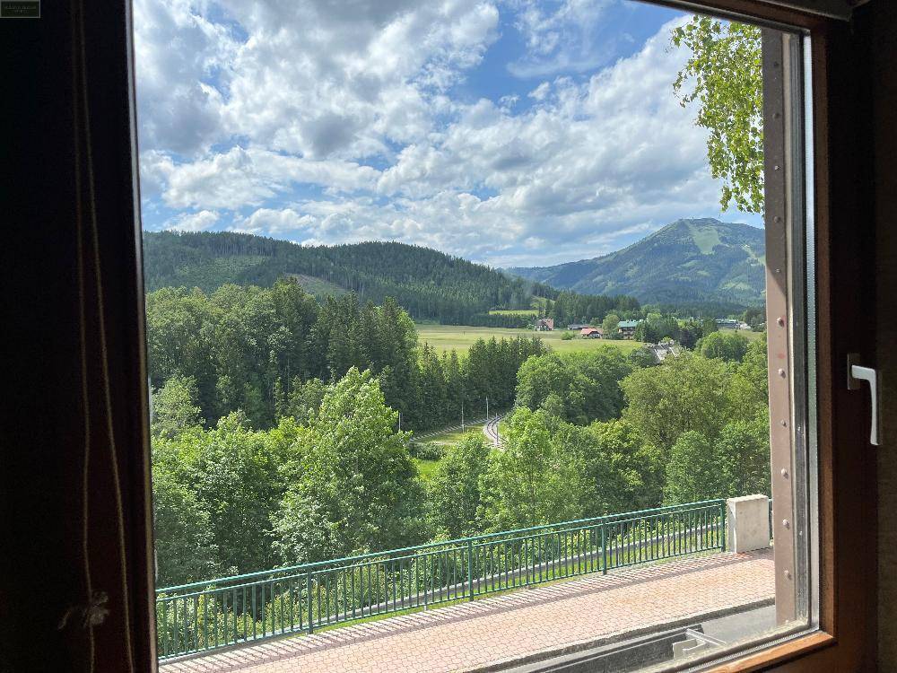 Weitläufiger Ausblick aus dem Fenster auf eine grüne Hügellandschaft und bewaldete Berge.