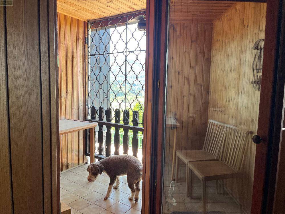 Überdachte Loggia mit Holzvertäfelung, Fliesenboden und einem Gitter, das den Blick freigibt.