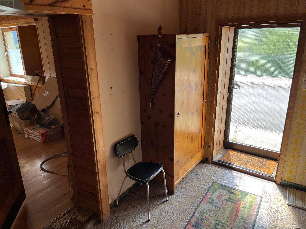 Eingangsbereich mit Fliesenboden, Holzschrank und Zugang zu einem weiteren Raum mit Lagerung.