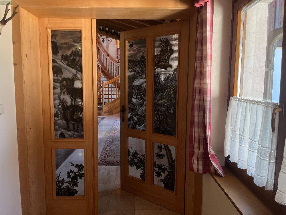 Holztüren mit dekorativen Glaseinsätzen, die den Blick auf eine elegante Holzwendeltreppe freigeben.